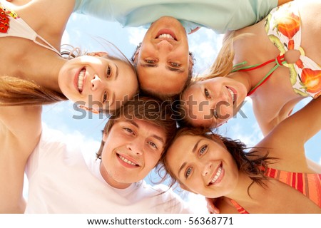 Below view of joyful teens embracing and looking at camera with smiles