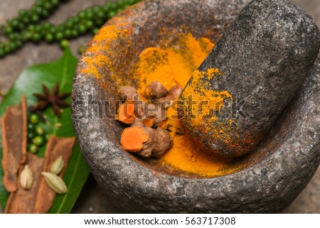 turmeric roots and powder in a mortar Kerala South India. Traditional Indian kitchen using vintage grinder for powdering spices which is used widely in curry and antiseptic Ayurveda treatments   Royalty-Free Stock Photo #563717308
