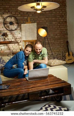 Loving couple sitting on sofa at home, using laptop computer.