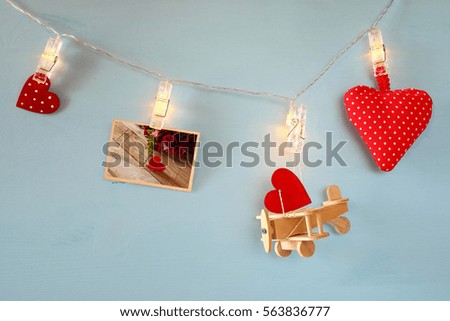 Valentines day background. Wooden plane, hearts and photograph hanging on garland with lights in front of blue background