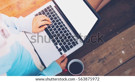 Beautiful girl uses Laptop and coffee cup in girl's hands sitting on a wooden floor, vintage tone