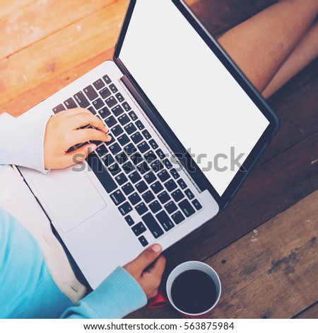 Beautiful girl uses Laptop and coffee cup in girl's hands sitting on a wooden floor, vintage tone