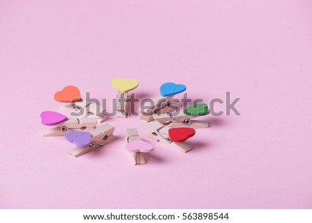 Colored heart shaped clothespins compose circle on pink background