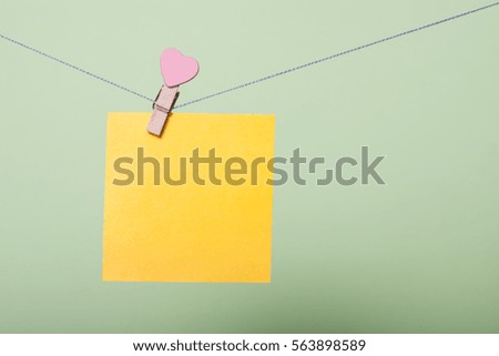 Yellow paper sheet on thread with heart shaped clothespin on greenery background