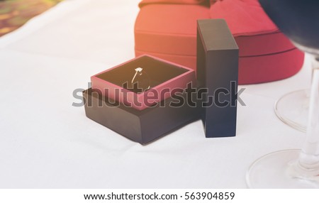 In selective focus of wedding engagement diamond rings lie in box red hreat and wine glass.On white floor.