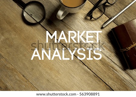 Top view of magnifier, a cup of coffee, eye glasses,  pen and notebook written with MARKET ANALYSIS on wooden background. A business concept.