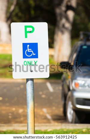 Close up parking sign reservation for disabled driver or person, wheelchair symbol on blue, car in blurred background, copy space.
