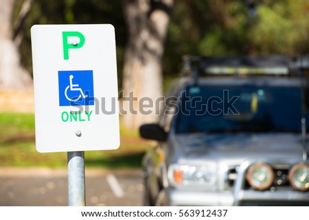 Close up parking sign reservation for disabled driver or person, wheelchair symbol on blue, car in outdoor blurred background, copy space.