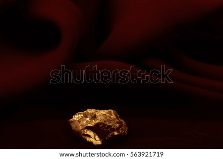 |Golden nugget on dark red silk texture background.