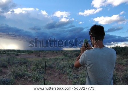 Man taking a picture on a camera phone of a huge storm cell in Namibia 