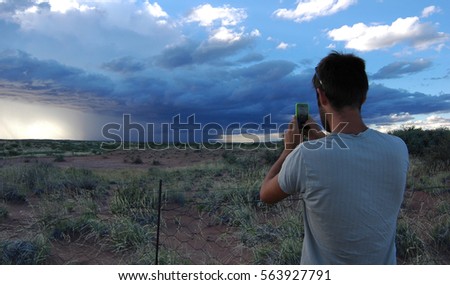 Man taking a picture on a camera phone of a huge storm cell in Namibia 