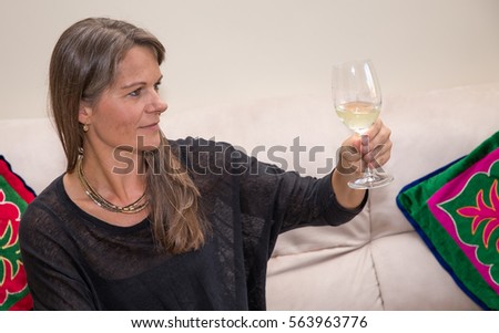 Middle aged woman enjoying a glass of white wine on a beige couch.