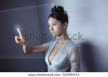 Young pretty asian female touching digital hologram screen. Future woman concept art. Fashion futuristic young attractive multi-racial Asian Caucasian model with futuristic make-up indoors. Copy space
