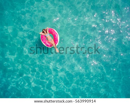 Aerial view of young brunette woman swimming on the inflatable big donut in the transparent turquoise sea. Top view of slim lady relaxing on her holidays in Thailand, Phuket, Andaman sea. Royalty-Free Stock Photo #563990914