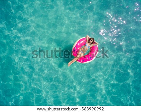 Aerial view of young brunette woman swimming on the inflatable big donut in the transparent turquoise sea. Top view of slim lady relaxing on her holidays in Thailand, Phuket, Andaman sea.