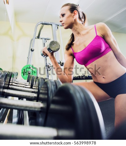 portrait of athlete girl hold metal barbell. Trim and beautiful woman in sportswear is training inside gym. Female raises dumbbells against mirror. Portrait of pretty girl training in gym room space. 