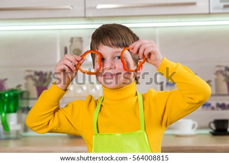 Funny boy with sliced paprika on eyes in the kitchen interior