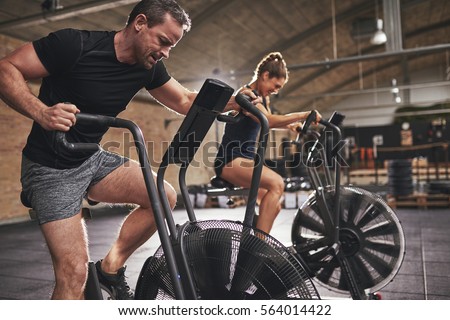 Young man and woman wearing training hardly on cycling machines in light spacious gym. Royalty-Free Stock Photo #564014422