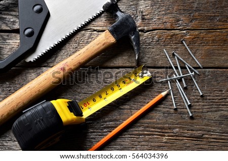 A top view image of an old hammer, saw blade, tape measure, and pencil. 