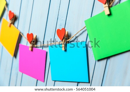 Colored paper sheets on thread with heart shaped clothespin blue wooden background