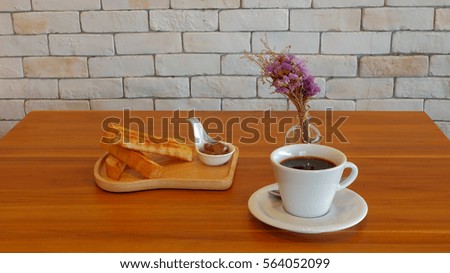Tasty and good aroma black coffee in white cup and toast with chocolate on wood table and white brick wall in a coffee corner in a garden, good environment for relaxation with friend, family or lovers