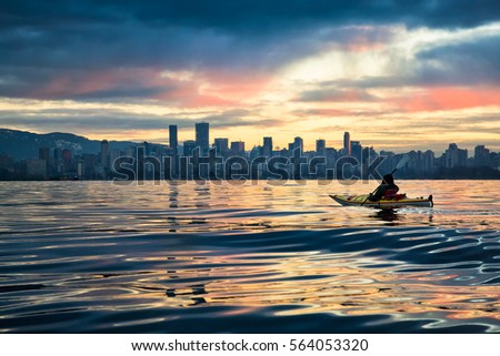 Man kayaking in front of Downtown Vancouver, BC, Canada. Picture taken during a cloudy winter sunrise.