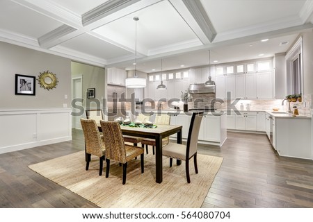 Lovely craftsman style dining and kitchen room interior with coffered cealing over rustic wooden dining table surrounded by wicker chairs. Northwest, USA
