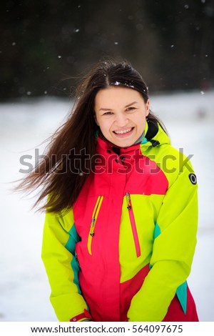 Lovely young woman brunette in a bright jacket on walk in winter day. It is snowing. The woman stands without headdress and joyfully laughs. Snowflakes lie on dark hair.