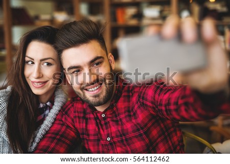 Couple in cafeteria, taking a selfie of themselves with smartphone.
