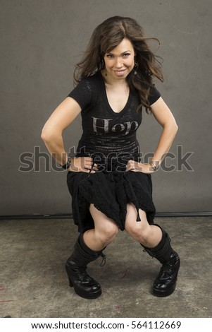 Young caucasian woman with brown hair, a black top, black cotton skirt, and tall black leather boots	