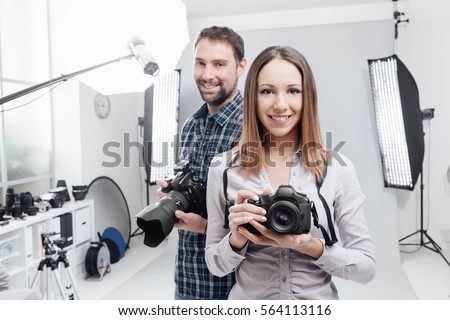Smiling young professional photographers posing in the studio, they are holding digital cameras