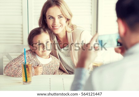 family, parenthood, technology and people concept - happy mother, father and little girl having dinner and taking picture by smartphone at restaurant