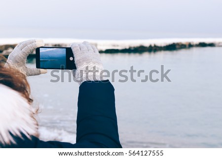 Girl taking pictures of the beach on a mobile phone in winter, close-up