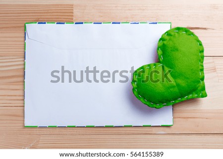 Green homemade heart on a love letter on Valentine's Day. Pantone greneery color theme. Blank envelope. Natural wooden table. Copy space.