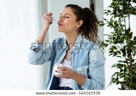 Portrait of beautiful young woman eating yogurt at home. Royalty-Free Stock Photo #564161938