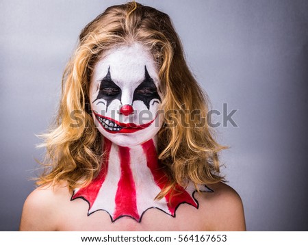 Portrait of a blond girl made up in joker with a fake smile on half the face and lowered eyes