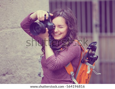 cheerful smiling girl photographer holding camera in hands and photographing in city
