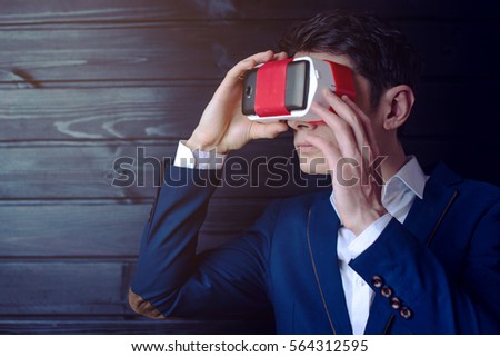 Attractive Young businessman in suit uses a colorful virtual reality glasses on a dark wooden background