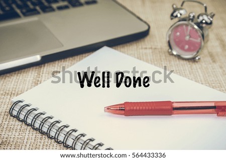 Wording WELL DONE on notebook with laptop, pen and clock on wooden table. Motivation and positive wishes concept
