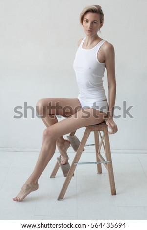 Young beautiful girl with a great figure sits on a stool in a white room. Model tests. Sports figure
