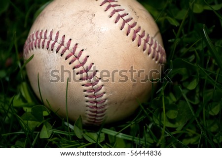 Closeup of an aged and worn hardball or baseball laying in the green grass. Shallow depth of field.