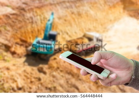 Man use mobile phone, blur image of excavator and truck in mining as background.