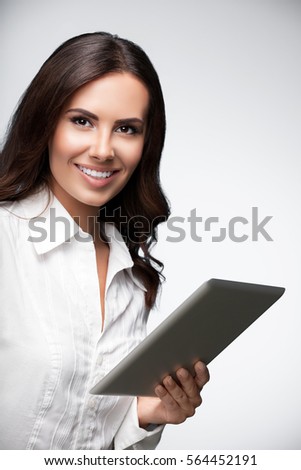 Portrait of happy smiling beautiful young brunette businesswoman using no-name tablet pc, over grey background. Success in business concept studio shot. 
