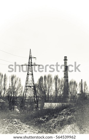 Factory pipe and high voltage pole covered snow. Monochrome photo.