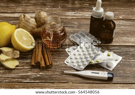Ginger, lemon, honey and  different drugs  with thermometer on wooden background.Alternative remedies and traditional pills to treat colds and flu. Natural medicine vs conventional medicine concept Royalty-Free Stock Photo #564548056