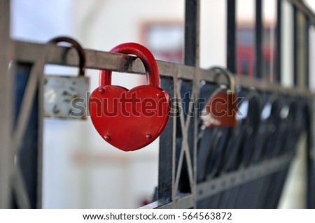 Black metal fence with hanging red closed padlock in the shape of heart close up.  