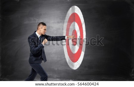 Businessman is hitting with a fist a target on black background of concrete wall. Making money. Goals achievement. Business advancement Royalty-Free Stock Photo #564600424