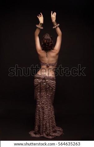 Oriental beauty with a slender figure and a narrow waist. View from the back . Hands raised up. Royalty-Free Stock Photo #564635263