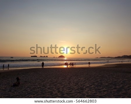 Girl playing in sand and people walking on the beach by sunset - Ixtapa, Mexico.