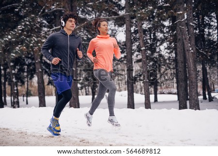 Photo of a two athletic people running in the forest on a winter day.